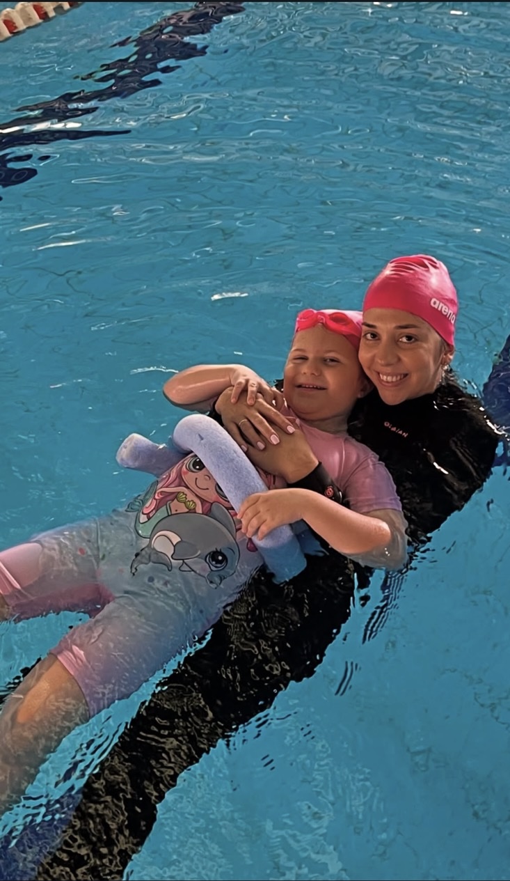 Θεραπεύτρια υποστηρίζει κορίτσι σε άσκηση ισορροπίας στο νερό